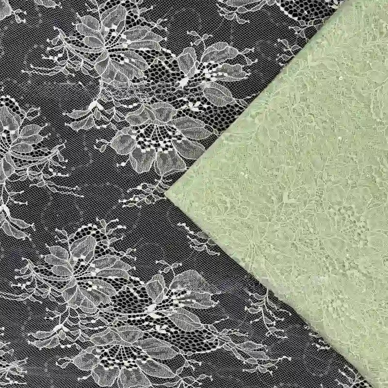 Le tissu dentelle vert pâle pailleté avec paillettes de Longan Craft France est superposé à de la dentelle noire ornée de fleurs blanches audacieuses et d'un motif floral subtil - idéal tissu dentelle pour robes et lingerie.