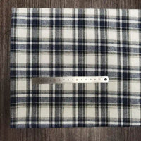 A piece of Tissu en flanelle à carreaux colorés Longon Craft France, une matière polyester-coton ultra-douillette, est posé sur une surface en bois. Un mètre ruban indique environ 15 cm sur le tissu confortable pour l'automne.