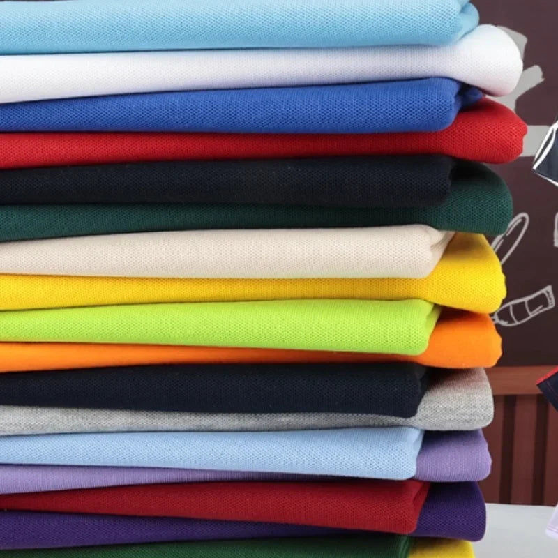 Pile de tissus pliés de différentes couleurs unies, dont le blanc, le bleu, le rouge, le vert, le jaune, l'orange, le noir, le gris et le violet, soigneusement empilés et disposés sur une surface plane.