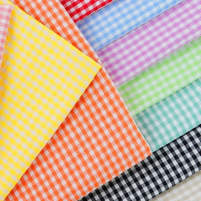 Une sélection de tissus vichy est disposée de manière à se chevaucher. Les tissus présentent un motif à carreaux de différentes couleurs, notamment orange, jaune, rose, rouge, bleu, violet, vert, blanc, noir et sarcelle.