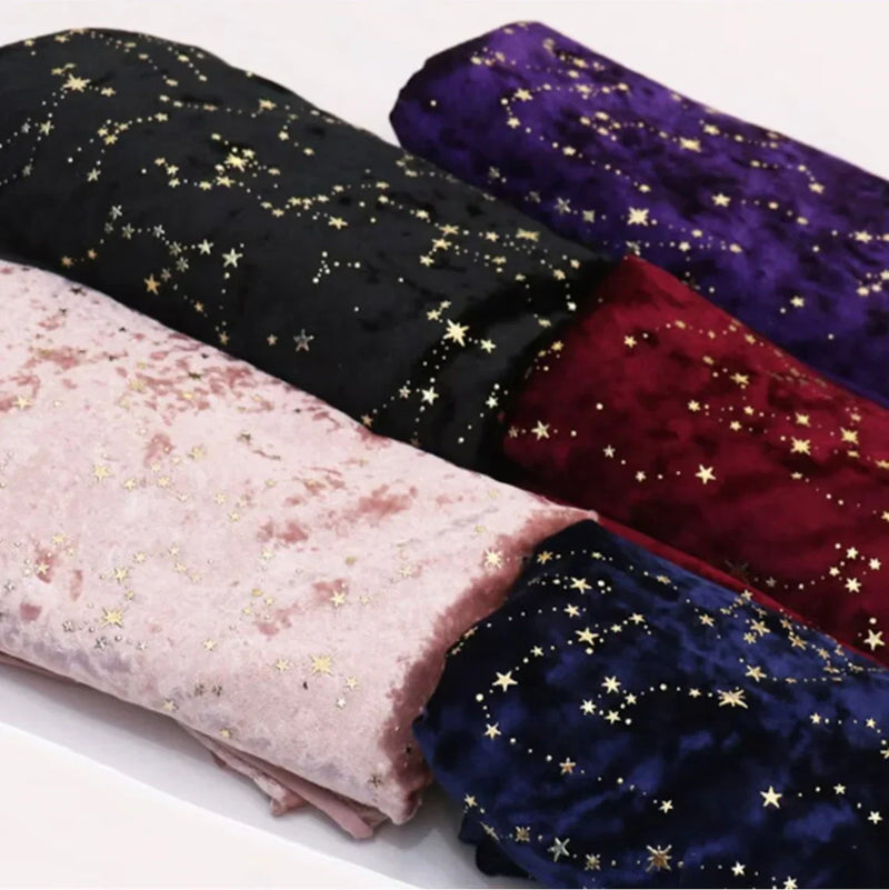 Quatre rouleaux de tissu de velours rose, noir, rouge et bleu foncé, chacun décoré d'un motif de petites étoiles dorées, sont disposés côte à côte sur une surface blanche.
