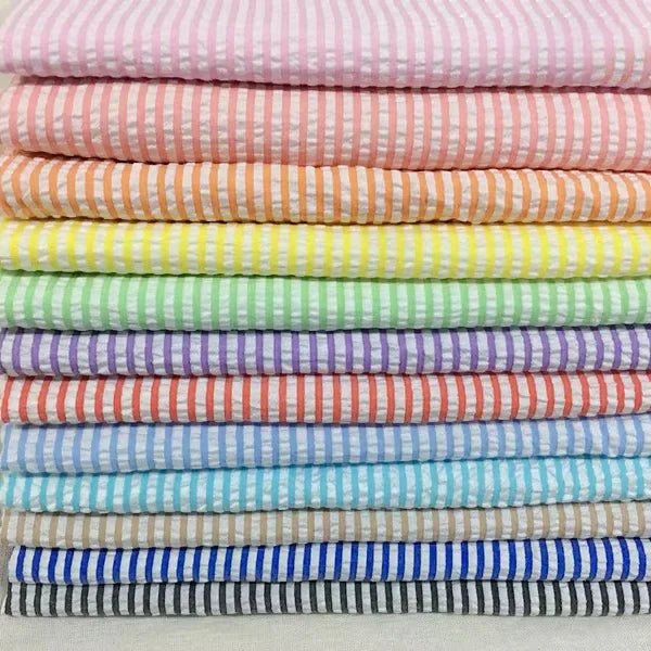 Une pile bien empilée de tissus rayés de différentes couleurs pastel et vives, disposés en dégradé du rose en haut au bleu foncé en bas.