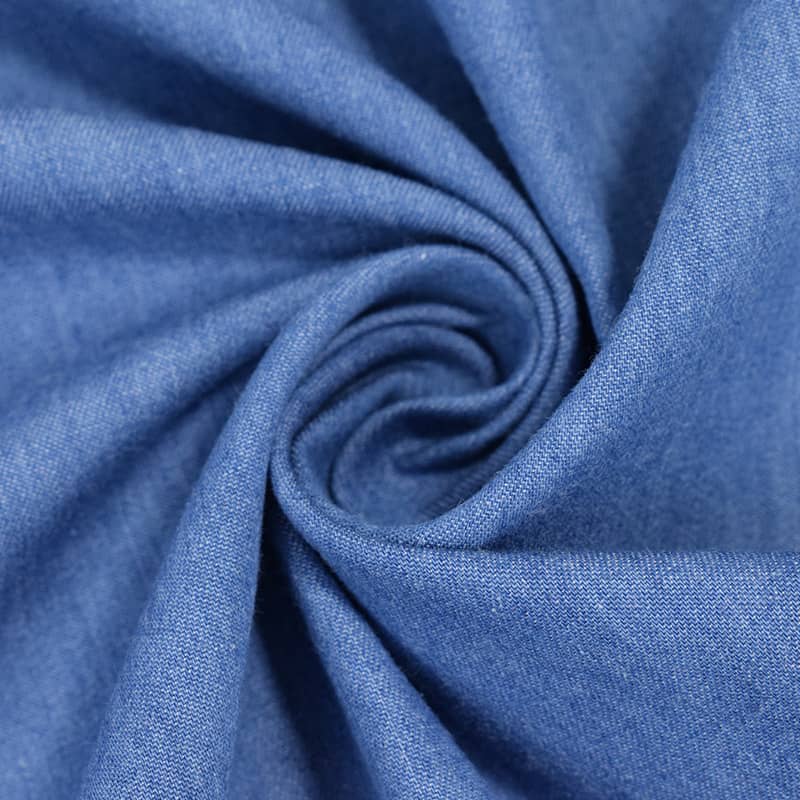 Gros plan sur le Tissu jean 100% coton au mètre, denim léger 4,5 oz bleu clair de Longan Craft France, torsadé en spirale pour mettre en valeur la texture et le tissage de ce tissu de coton légèrement délavé.