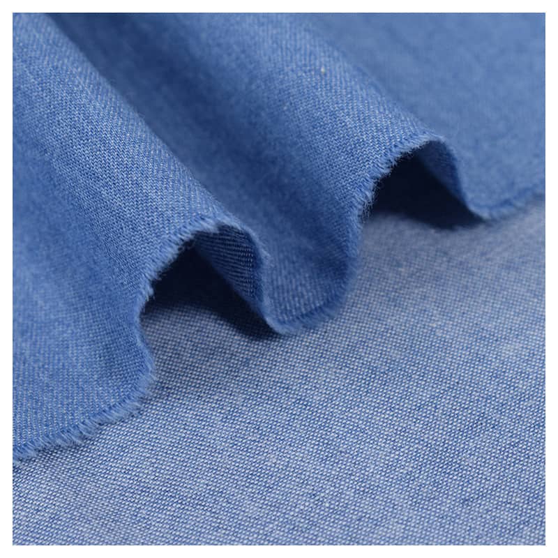 Un gros plan sur le Tissu jean 100 % coton au mètre, denim léger 4,5 oz bleu clair de Longan Craft France, met en évidence son tissage fin, sa texture lavée douce, ses plis délicats et son bord subtilement effiloché.