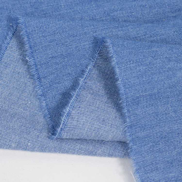 Un gros plan du Tissu jean 100% coton au mètre, denim léger 4,5 oz bleu clair de Longan Craft France, montre ses bords bruts et effilochés et ses plis en zigzag qui mettent en valeur le tissage et la texture de ce tissu jean en coton bleu clair délavé.