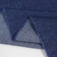 Un gros plan du Tissu jean 100 % coton au mètre (denim léger 4,5 oz bleu clair) de Longan Craft France montre les bords coupés en zigzag et le tissage superposé, révélant à la fois le recto et le verso de ce tissu denim en coton lavé.