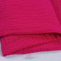 Gros plan sur deux pièces de Tissu double gaze 100 % coton au mètre rose vif de Longan Craft France, empilées pour mettre en valeur le tissage doux et léger et la surface texturée, parfaits pour les vêtements et les accessoires.