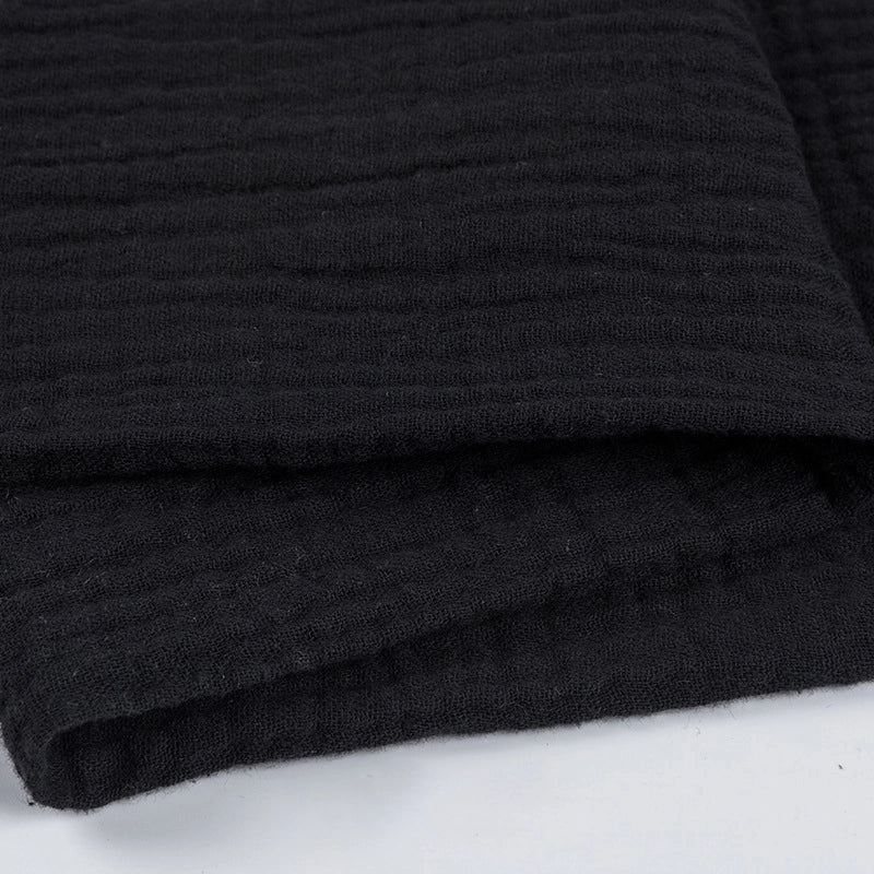 Gros plan sur Tissu double gaze 100% coton de Longan Craft France, un tissu texturé noir plié avec un subtil motif horizontal ligné sur une surface blanche - léger et doux, idéal pour les vêtements et les accessoires.