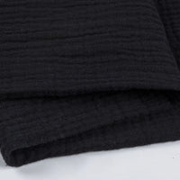 Gros plan sur Tissu double gaze 100% coton de Longan Craft France, un tissu texturé noir plié avec un subtil motif horizontal ligné sur une surface blanche - léger et doux, idéal pour les vêtements et les accessoires.