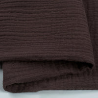 Un gros plan du Tissu double gaze 100 % coton au mètre de Longan Craft France montre son tissu texturé brun foncé aux rayures subtiles. Léger, doux et respirant, il est parfait pour les vêtements et les accessoires.