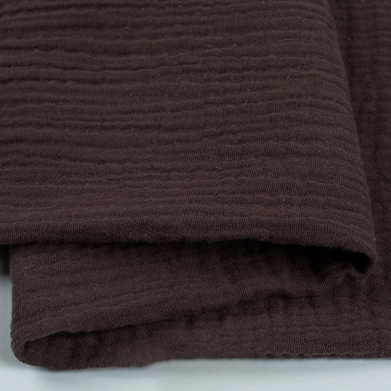 Un gros plan du Tissu double gaze 100 % coton au mètre de Longan Craft France montre son tissu texturé brun foncé aux rayures subtiles. Léger, doux et respirant, il est parfait pour les vêtements et les accessoires.