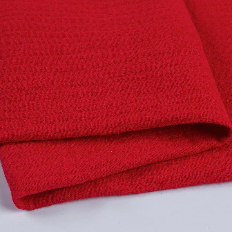 Gros plan sur le tissu double gaze 100 % coton au mètre de Longan Craft France, un tissu léger et doux idéal pour les vêtements et les accessoires, montrant le tissage texturé rouge et les fines lignes horizontales sur une surface gris clair.