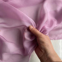 Une main pince délicatement la mousseline de soie de mûrier de luxe au mètre de Longan Craft France, un tissu naturel, léger et pur pour l'habillement, révélant sa texture lisse, sa qualité translucide et sa brillance subtile.