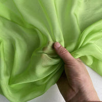 Une main recueille délicatement la luxueuse mousseline de soie de mûrier de Longan Craft France en vert clair, soulignant la translucidité naturelle du tissu et sa texture douce et délicate, vendue au mètre pour des vêtements purs et légers.