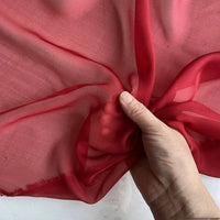 Une main présente la texture transparente et légère de la Mousseline de soie de mûrier de luxe au mètre de Longan Craft France, une mousseline de pure soie de mûrier naturelle idéale pour l'habillement, sur un fond neutre.
