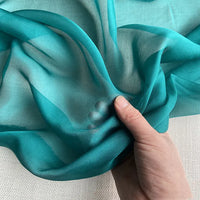 Une main froisse la Mousseline de soie de mûrier de luxe au mètre de Longan Craft France, révélant sa texture légère et translucide, idéale pour les vêtements élégants.