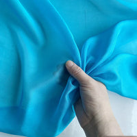 Une main tient et rassemble délicatement la Mousseline de soie de mûrier de luxe de Longan Craft France, une mousseline de soie de mûrier naturelle, légère et transparente, vendue au mètre, idéale pour les vêtements de luxe.