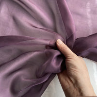Une main fronce la Mousseline de soie de mûrier de luxe de Longan Craft France, créant de légers plis et des ombres sur le tissu de soie naturelle transparent et léger, parfait pour des vêtements purs et élégants.
