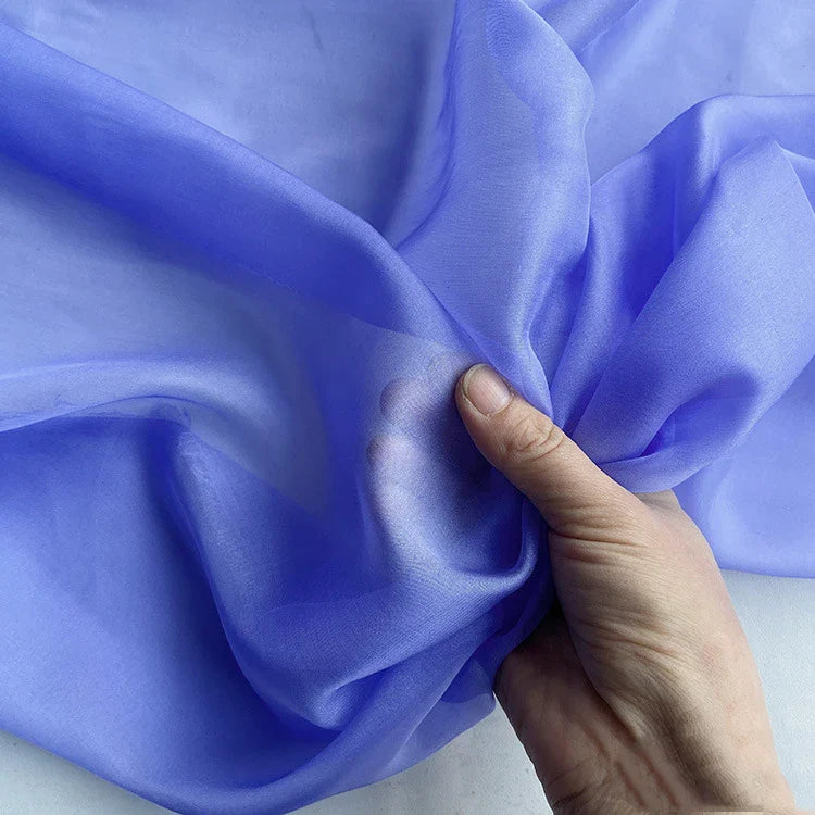 Une main tient la Mousseline de soie de mûrier pourpre clair de Longan Craft France, une mousseline de soie naturelle lisse et translucide vendue au mètre, luxueusement légère et parfaite pour les vêtements élégants.