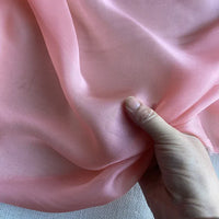 Une main présente la luxueuse mousseline de soie de mûrier de Longan Craft France - une mousseline rose pâle, naturellement pure et douce - sur un fond clair, idéale pour créer des robes et des vêtements de luxe.