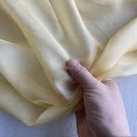 Une main présente la luxueuse mousseline de soie de mûrier jaune pâle de Longan Craft France - Mousseline de soie de mûrier - sur une toile de fond légèrement texturée, montrant son drapé naturel et léger pour la confection de robes élégantes.