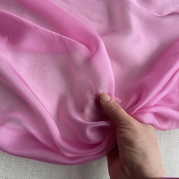 Une main présente la texture délicate et translucide de la Mousseline de soie de mûrier de luxe au mètre de Longan Craft France - une mousseline de soie de mûrier naturelle et légère, idéale pour les vêtements de luxe - sur un fond neutre.