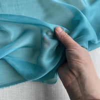 Une main présente la luxueuse mousseline de soie de mûrier de Longan Craft France, un tissu naturel bleu clair semi-transparent au mètre, doux, transparent et élégant, idéal pour les vêtements haut de gamme.