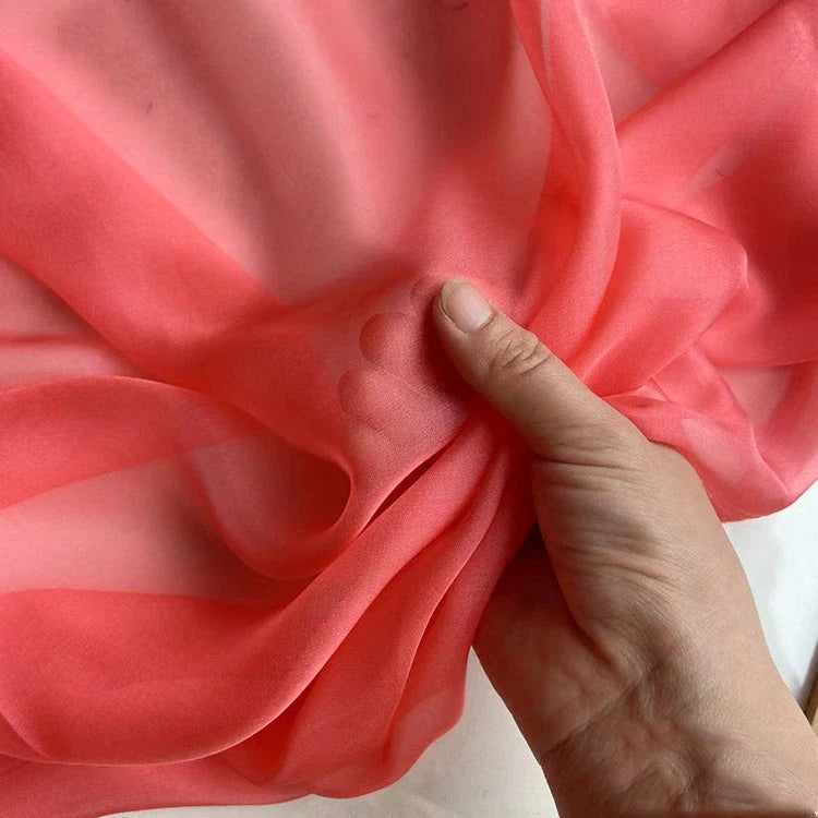 Une main rassemble délicatement la Mousseline de soie de mûrier de luxe au mètre de Longan Craft France, révélant son tissu naturel diaphane, léger et translucide, parfait pour créer des vêtements élégants.