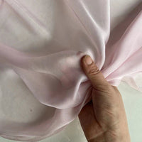 La Mousseline de soie de mûrier de luxe au mètre, rose pâle, de Longan Craft France, est tenue par une main qui en fait des bouquets, mettant en valeur sa pureté naturelle, sa légèreté et sa qualité translucide, idéale pour la confection de vêtements.