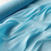 Gros plan sur le Tissu soie et lin 14 mamans au mètre de Longan Craft France, un organza de soie de mûrier à la texture lisse et légèrement brillante de couleur bleu clair, présenté en plis souples et en ondulations avec un bord roulé visible.