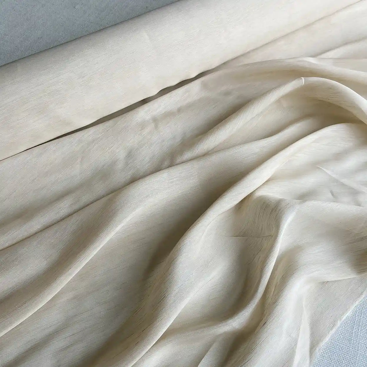 Un gros plan du Tissu soie et lin 14 mamans au mètre de Longan Craft France montre des plis doux et une surface lisse et légèrement texturée. Cet organza de soie de mûrier vibrant est idéal pour les projets d'été.