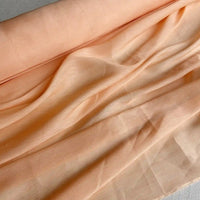 Un gros plan de Tissu soie et lin 14 mommes de Longan Craft France, en pêche, avec une texture douce et des plis naturels, met en valeur l'élégance et la couleur vibrante de cet organza de soie de mûrier, parfait pour l'été.