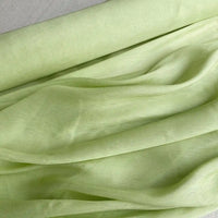 Gros plan sur Longan Craft France Tissu soie et lin 14 mommes, organza de soie de mûrier d'un vert clair vibrant, doucement drapé en plis doux avec une texture estivale délicate et légèrement froissée.