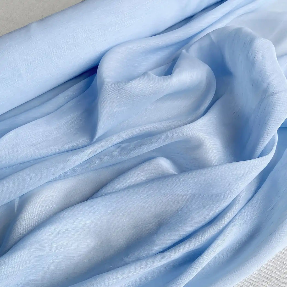 Gros plan sur Tissu soie et lin 14 mamans au mètre de Longan Craft France, un organza de soie et de lin de mûrier bleu clair, au lustre doux, au drapé et à l'étoffe amples, idéal pour les projets d'été.
