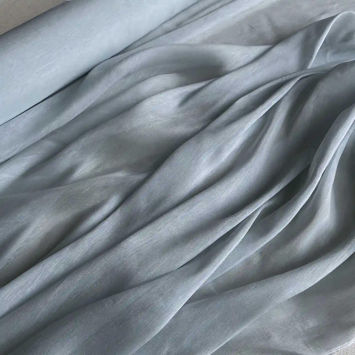 Un rouleau de Tissu soie et lin 14 mamans au mètre de Longan Craft France est étalé, montrant des plis lisses et une texture légèrement brillante et légère. Cet organza vibrant en mélange de soie de mûrier est idéal pour l'été et pour ceux qui recherchent un tissu de luxe.