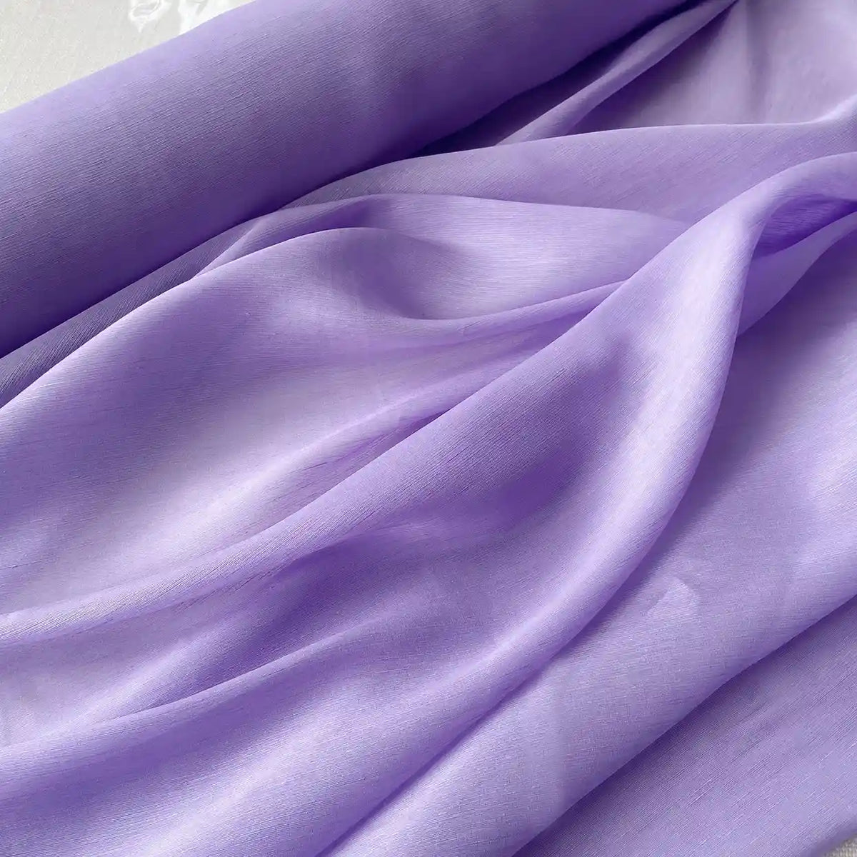 Tissu soie et lin 14 mommes au mètre de Longan Craft France, organza de mûrier aux couleurs vibrantes, est légèrement drapé et froncé pour révéler sa texture douce et fluide sous une lumière douce. Idéal pour l'été.