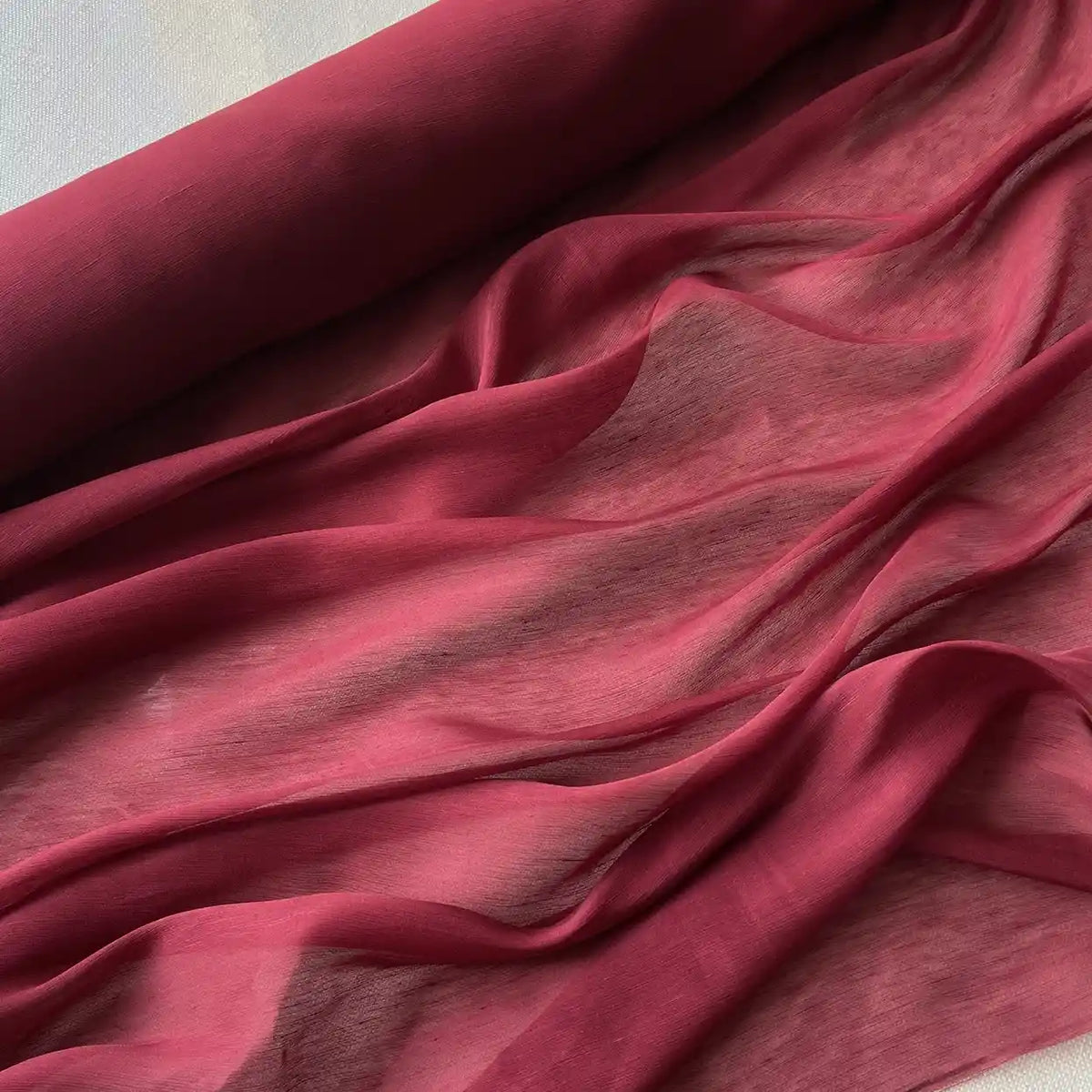 Gros plan sur le Tissu soie et lin 14 mamans au mètre de Longan Craft France en marron, un organza de soie de mûrier transparent et léger, drapé en plis doux avec une section roulée affichée sur le bord supérieur.