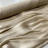 Un rouleau de Tissu soie et lin 14 mommes de Longan Craft France, un tissu soie-linen beige clair semi-transparent idéal pour l'été, est partiellement déroulé sur une surface plane, révélant sa texture lisse et ses plis doux.