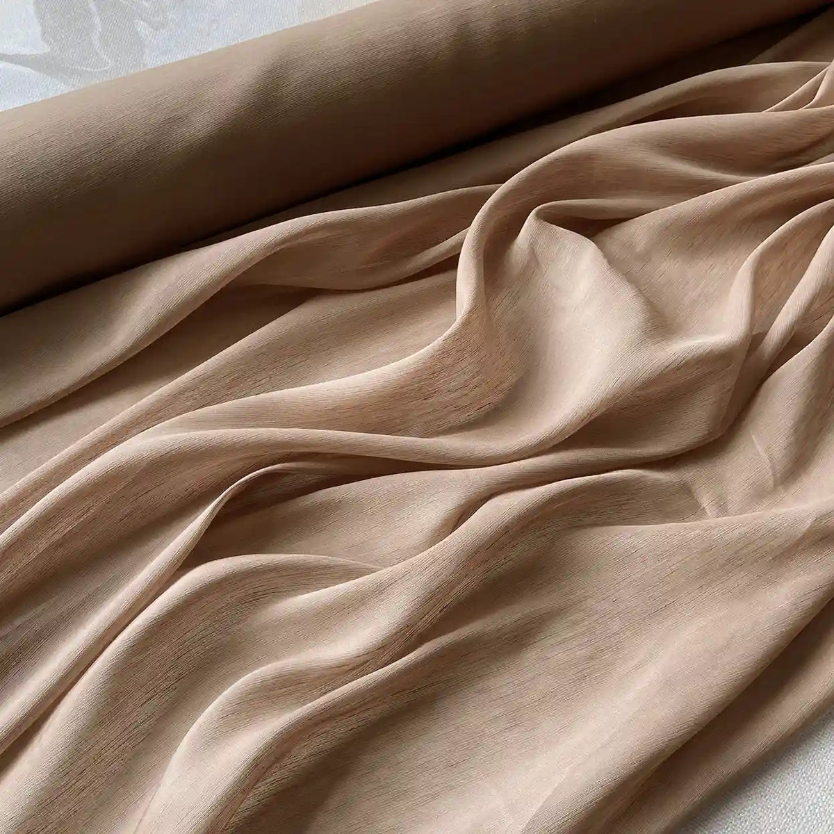 Gros plan sur Tissu soie et lin 14 mommes de Longan Craft France, un rouleau d'organza de soie de mûrier beige clair, partiellement déroulé avec des plis souples et des ombres douces, parfait pour les créations estivales.