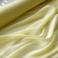 Gros plan sur le tissu soie et lin 14 mamans au mètre de Longan Craft France, un organza de soie de mûrier diaphane jaune clair aux plis doux et chatoyants, un tissu élégant et luxueux idéal pour l'été.