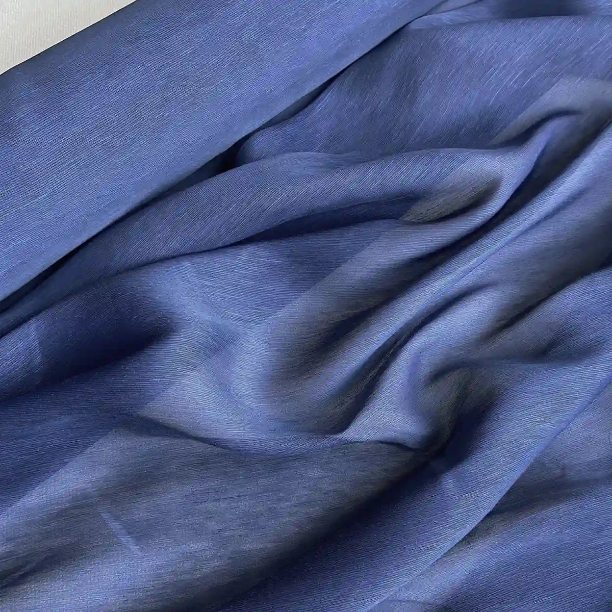 Un gros plan du Tissu soie et lin 14 mamans au mètre de Longan Craft France montre son organza bleu léger et transparent de soie de mûrier - délicat, semi-transparent, légèrement texturé et parfait comme tissu d'été luxueux.