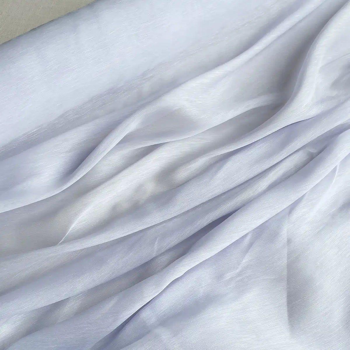 Un gros plan de Tissu soie et lin 14 mommes de Longan Craft France, d'un blanc doux et semi-transparent, montre des plis et des drapés doux, mettant en valeur la texture raffinée de l'organza de soie de mûrier - parfait pour les projets d'été.