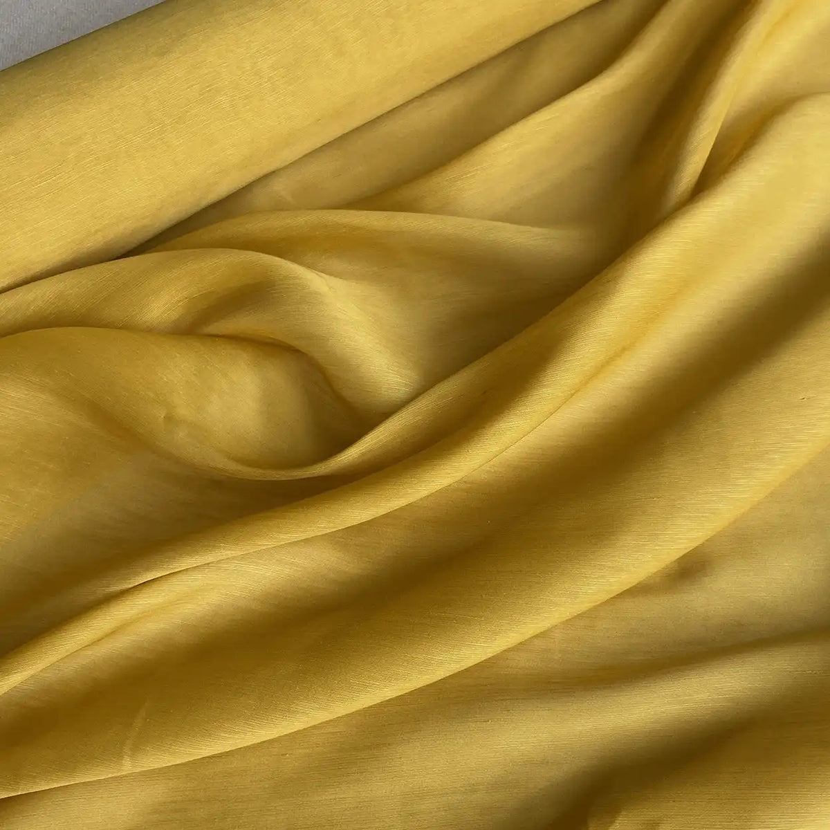 Gros plan sur Tissu soie et lin 14 mommes de Longan Craft France, qui présente des plis souples et une texture jaune vibrante et lisse. C'est l'organza d'été idéal étalé sur une surface plane.