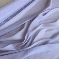Un gros plan du Tissu soie et lin 14 mommes de Longan Craft France montre un organza de soie de mûrier lisse et violet clair avec des plis doux qui créent des ombres douces - idéal pour l'été avec des couleurs vibrantes et une texture luxueuse.