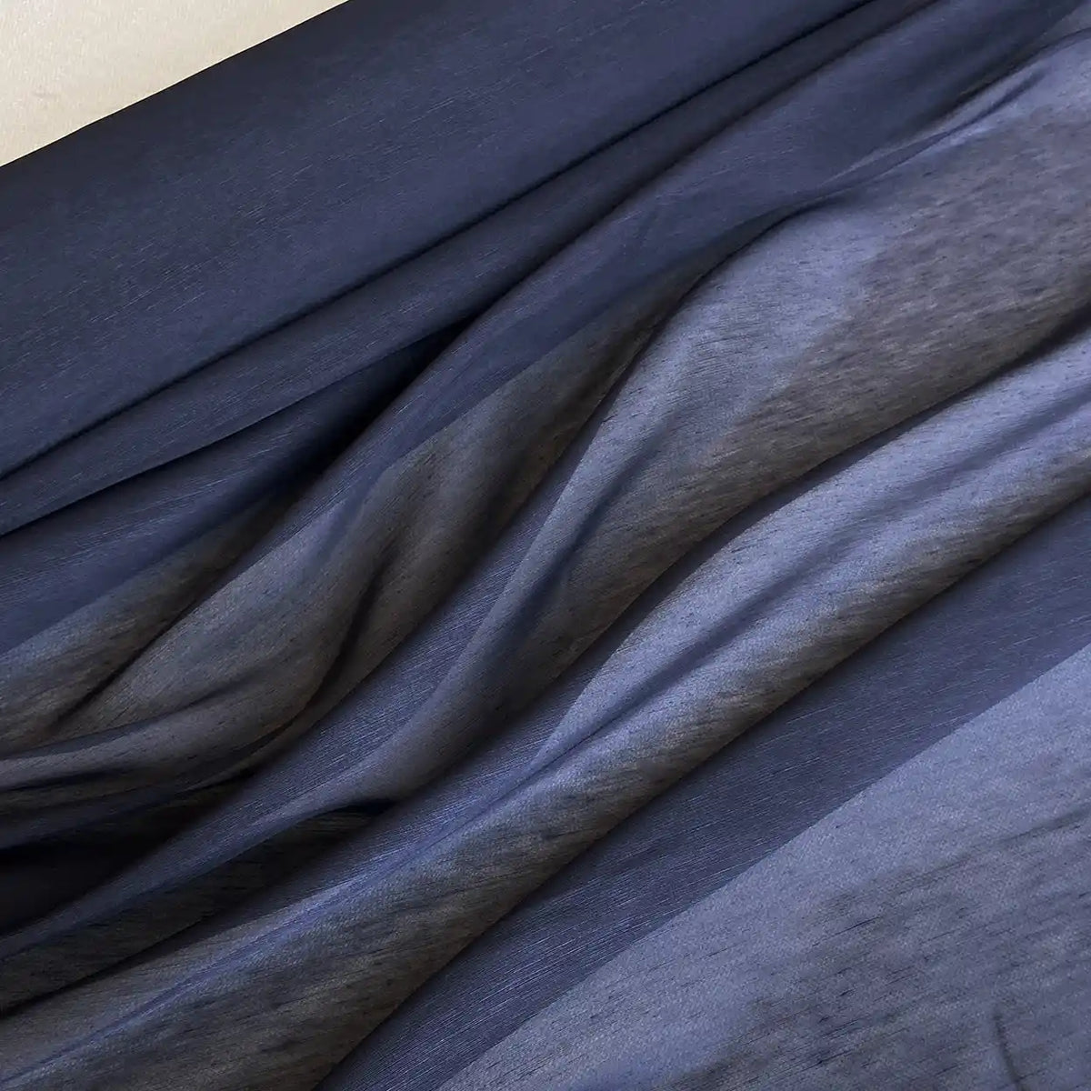 Un gros plan sur l'organza de soie et de lin de Longan Craft France (14 mommes/m), légèrement drapé en plis fluides, met en évidence sa texture semi-transparente et son jeu subtil de lumière - un tissu parfait pour l'été.