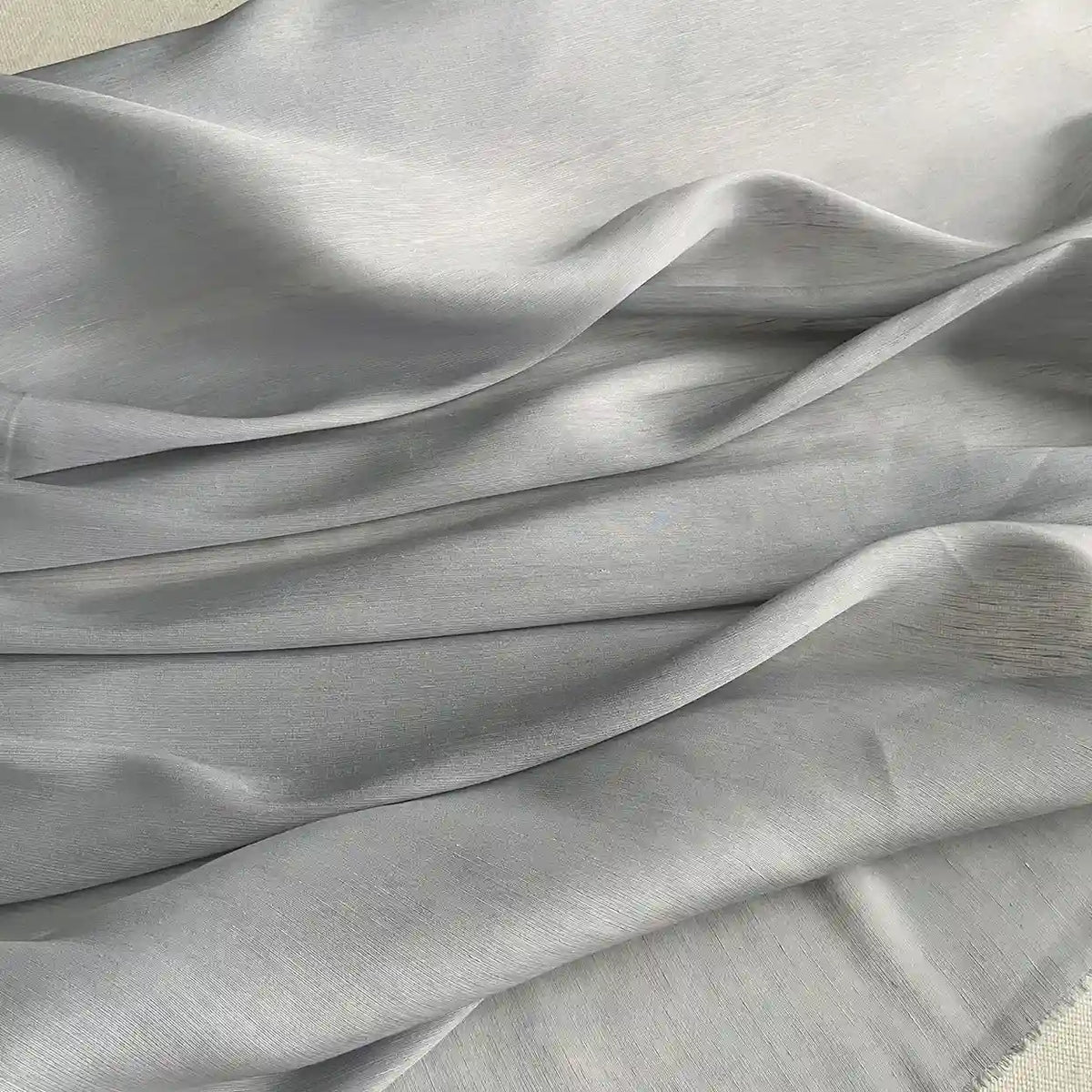 Un gros plan du Tissu soie et lin 14 mamans au mètre de Longan Craft France montre des plis délicats et une brillance subtile, soulignant le drapé élégant et la texture de cet organza de ver à soie luxueux et vibrant, idéal pour l'été.