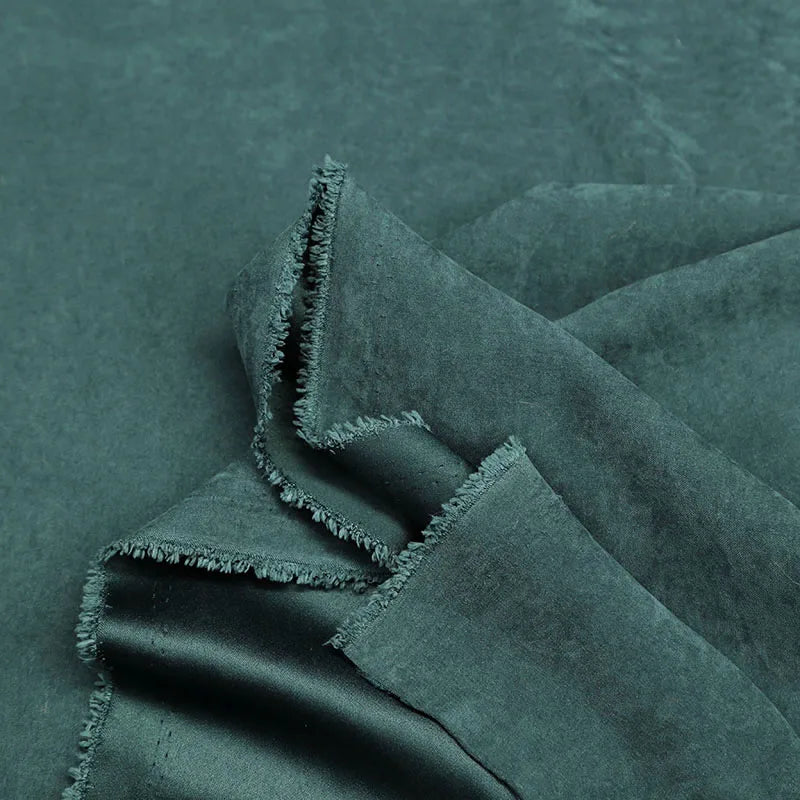 Gros plan sur des couches vert foncé de Microsuède polyester multicolore au mètre Longan Craft France, tissu peau de pêche brossée doux, aux bords effilochés-parfait pour la confection de vêtements et la décoration.