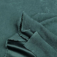 Gros plan sur des couches vert foncé de Microsuède polyester multicolore au mètre Longan Craft France, tissu peau de pêche brossée doux, aux bords effilochés-parfait pour la confection de vêtements et la décoration.