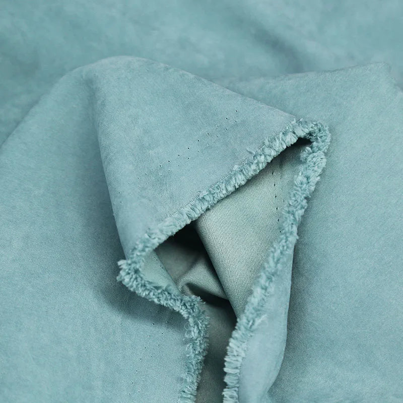 Gros plan sur Longan Craft France Microsuède polyester multicolore au mètre, montrant sa texture brossée en peau de pêche bleu clair, son toucher doux et son bord plié non fini et légèrement effiloché, idéal pour la confection de vêtements.