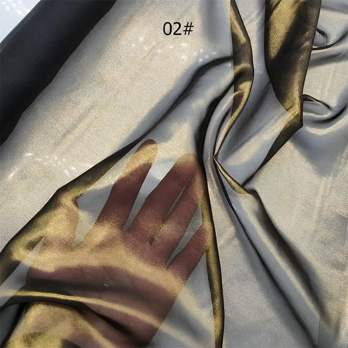 Une main sous du Tissu mousseline métallisé au mètre, noir et or, transparent et chatoyant, de Longan Craft France, montre sa transparence. Le numéro "02#" apparaît en haut de l'image.